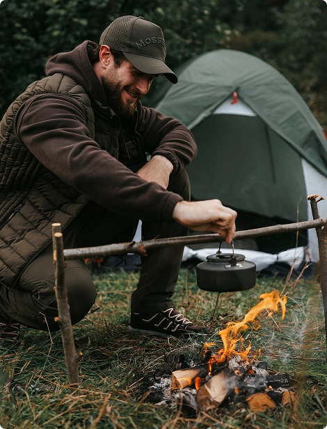 Рыбак готовит ужин в котелке на костре.