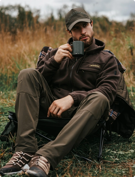Охотник отдыхает на складном стуле и пьет горячий чай.