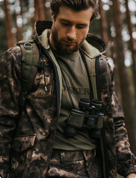 Охотник в камуфляже Mossberg с биноклем на груди.