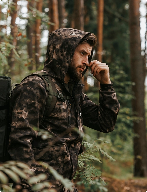 Охотник в камуфлированном костюме Mossberg в лесу.